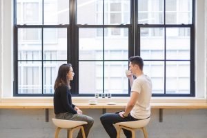 Two people talking a man and a woman in front of a large window